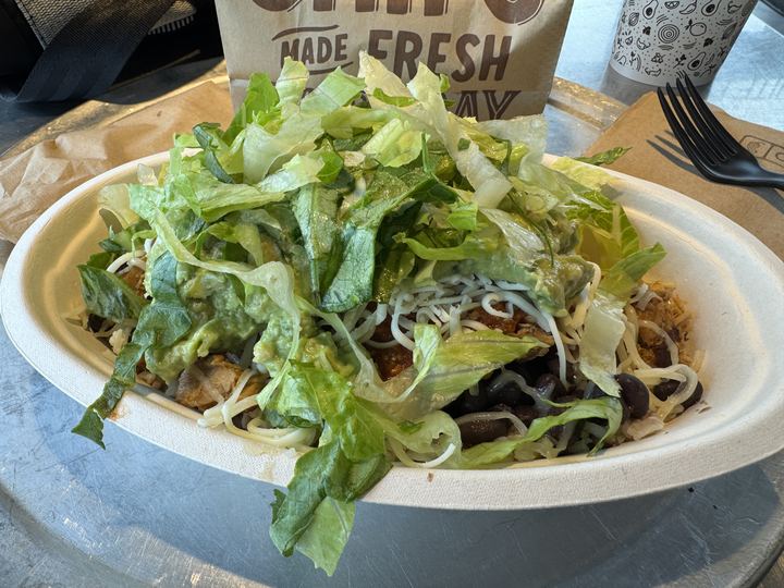 A burrito bowl with rice, beans, meat, salsa and guacamole
