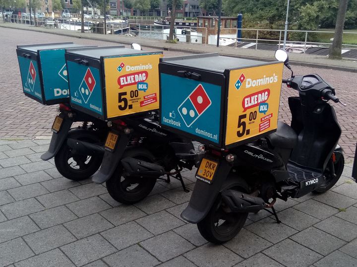 A row of pizza delivery scooters parked outside a shop